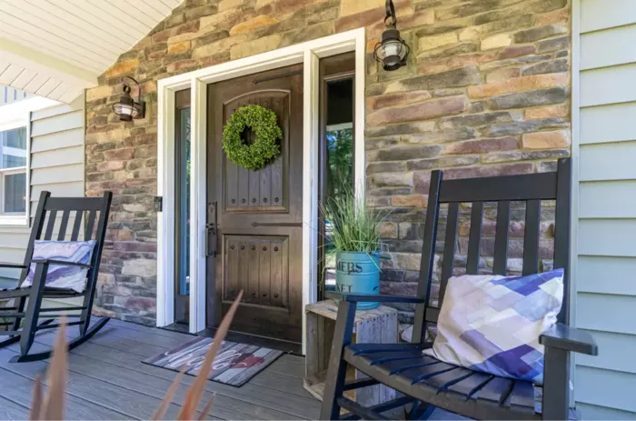 a front porch of a house with a stone wall and a chair and a wreath.